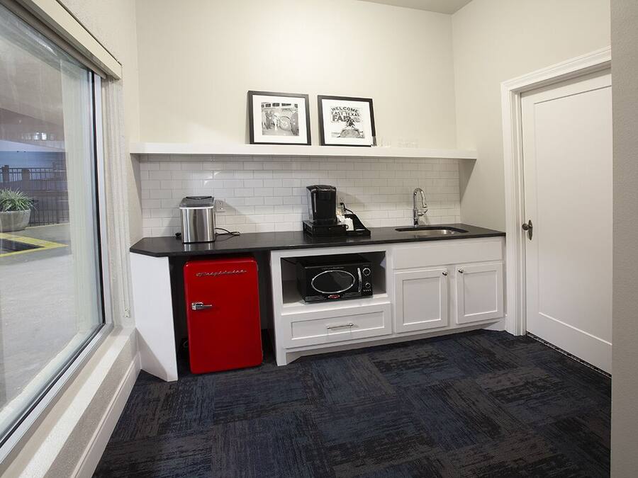 A compact kitchen with a red refrigerator, a coffee maker, and a microwave. There are two framed pictures on the wall and a window with a view of the outside.