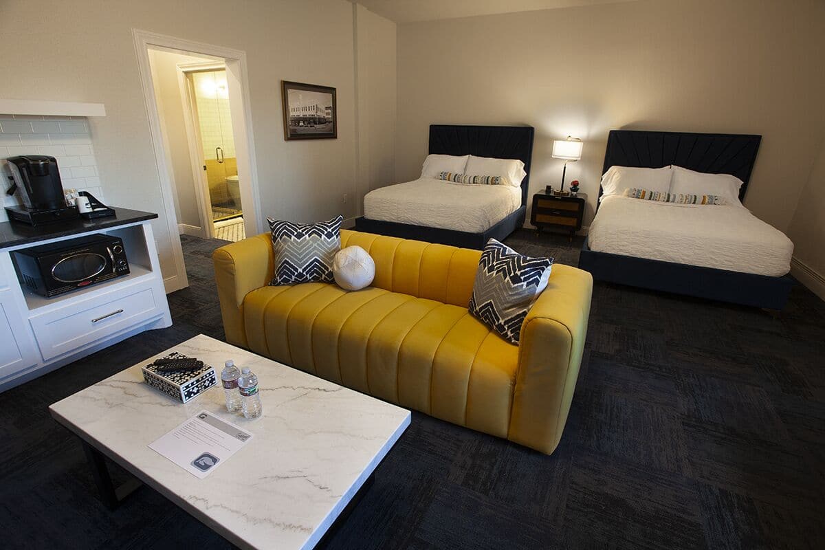 A hotel room with a yellow sofa, two beds with dark headboards, a small table with a coffee maker, and a microwave.