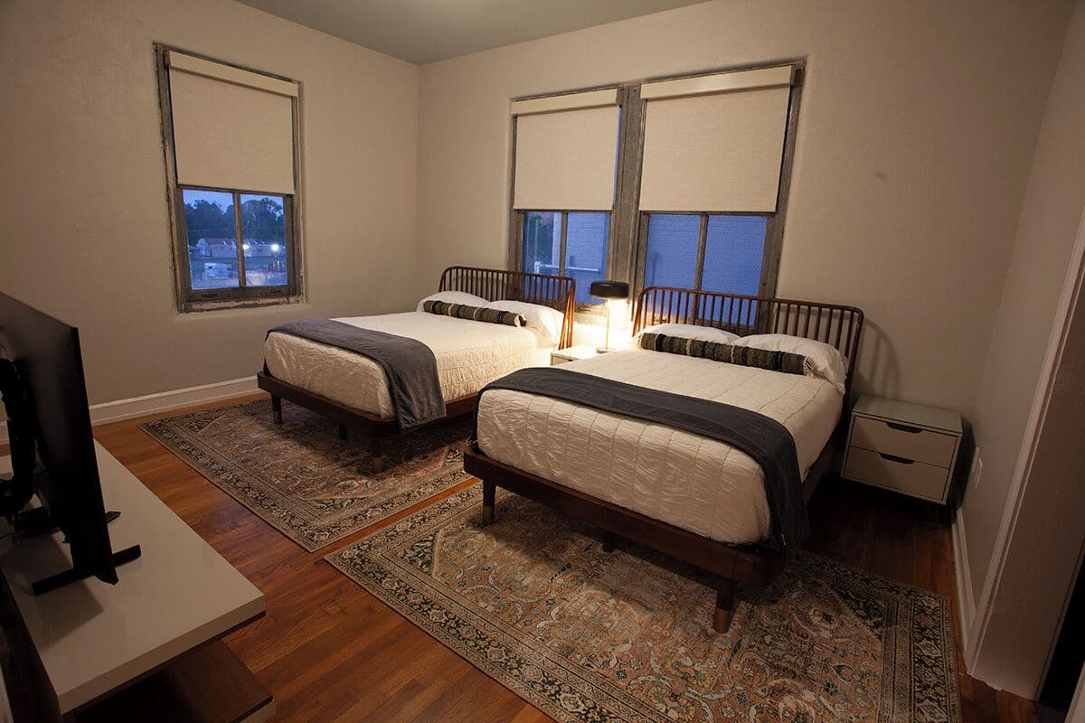 A bedroom with two beds, a nightstand, a desk, and a TV.