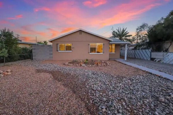 A single-story house with a flat roof and a small front yard with gravel and a few plants. - A Cozy Smart Home! (Tucson)