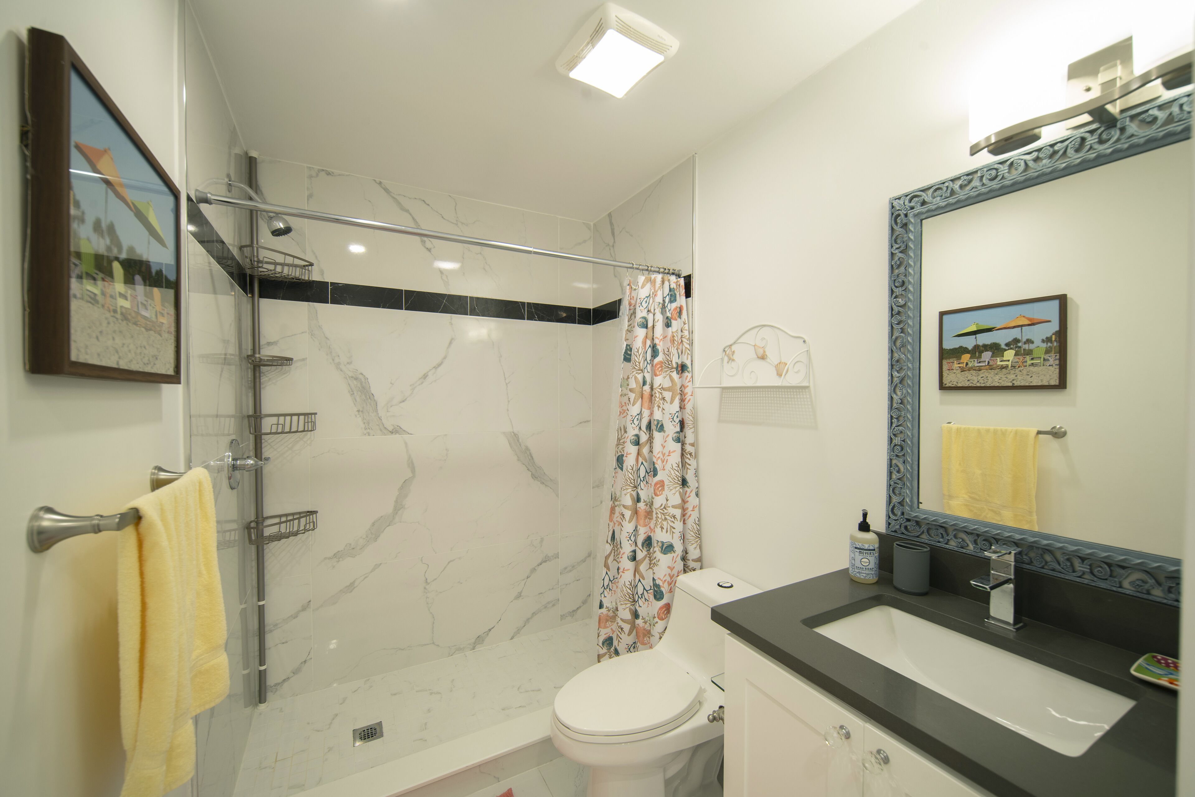 Une salle de bain équipée d’une douche, de toilettes, d’un lavabo et d’un miroir avec un cadre décoratif.