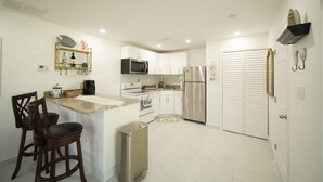 Una cocina moderna con armarios blancos, electrodomésticos de acero inoxidable y un pequeño comedor con dos sillas de madera.