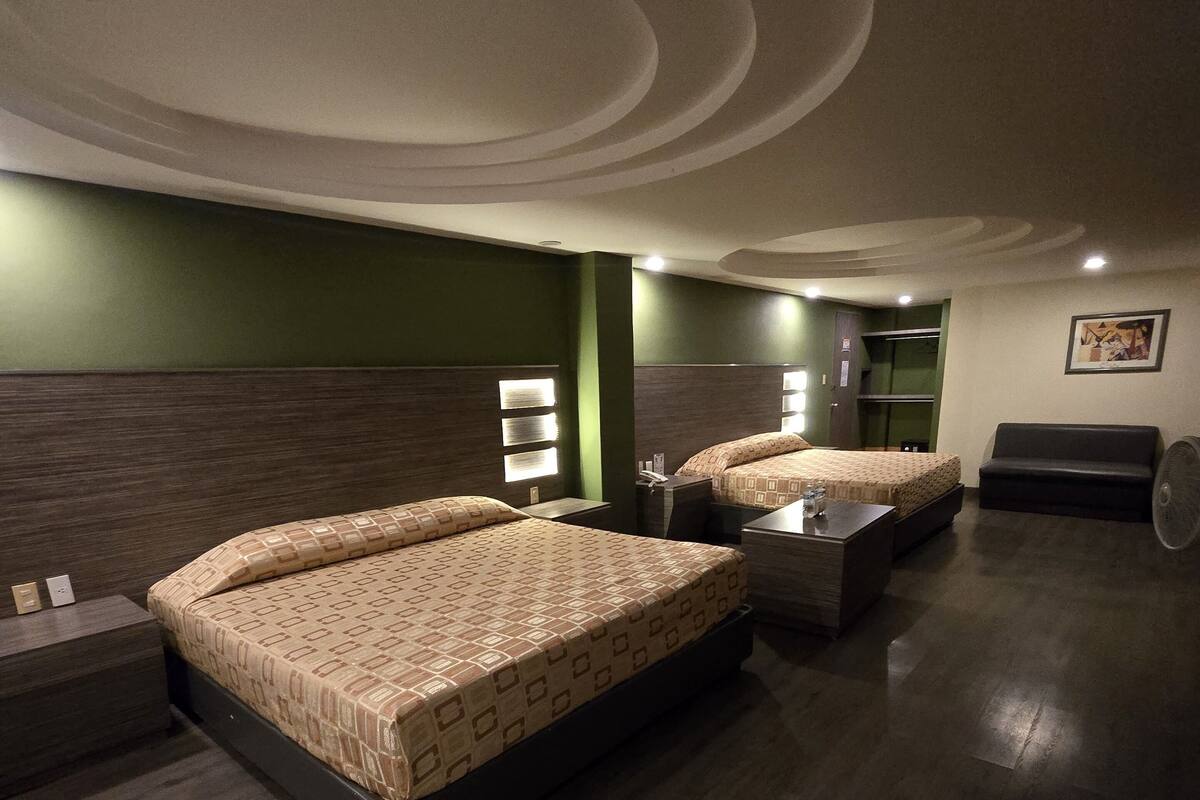 A hotel room with two beds, a sofa, a small table, and a fan.