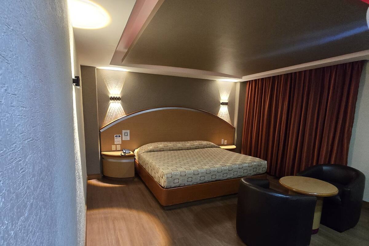 A bedroom with a bed, bedside lamps, a nightstand, a small round table, and a black chair.