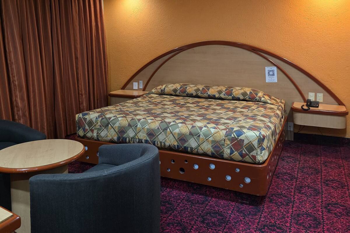 A hotel room with a bed, a round table, a chair, a nightstand, and a patterned carpet.