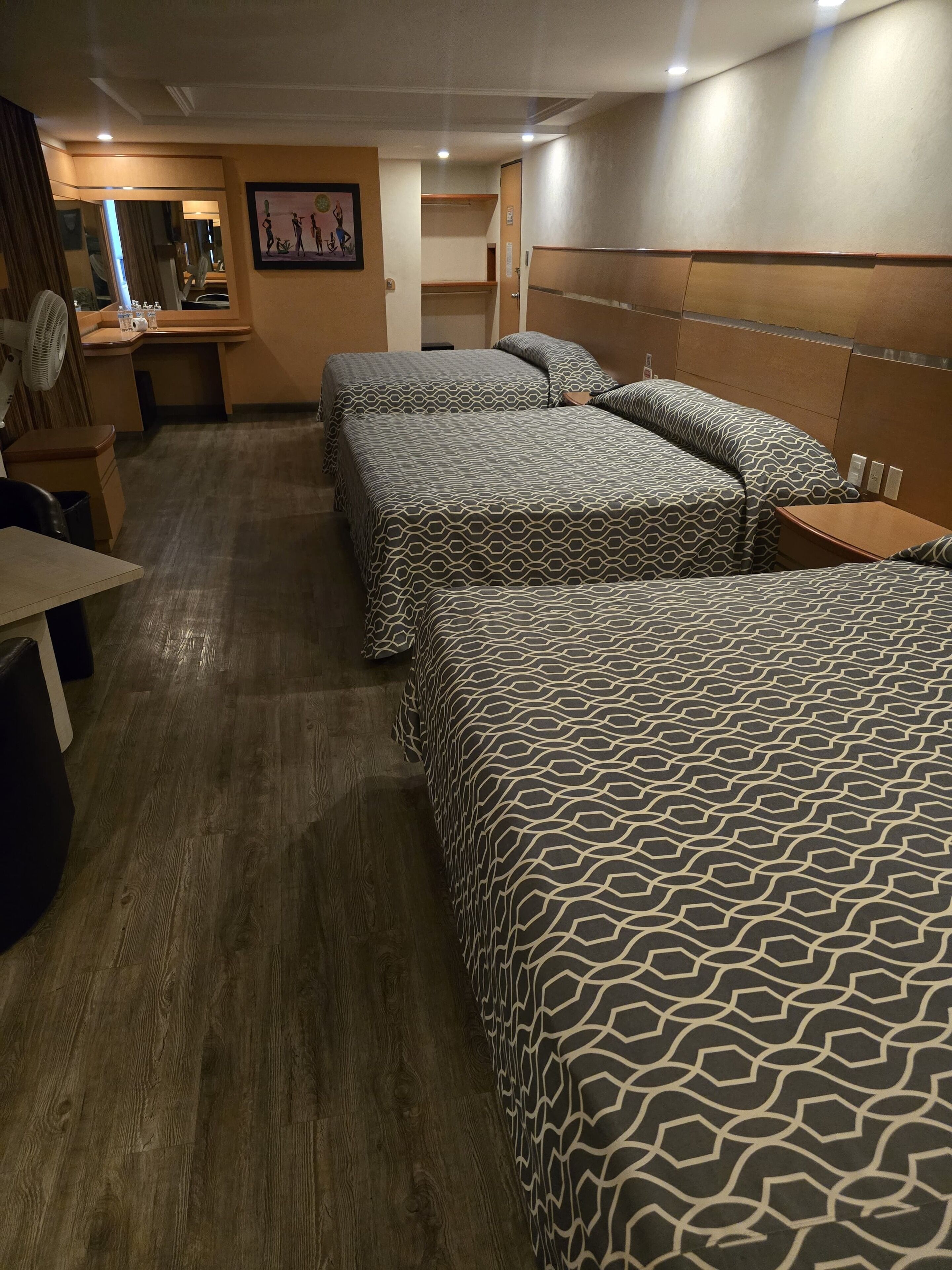 A hotel room with three beds, a desk, a chair, and a mirror.