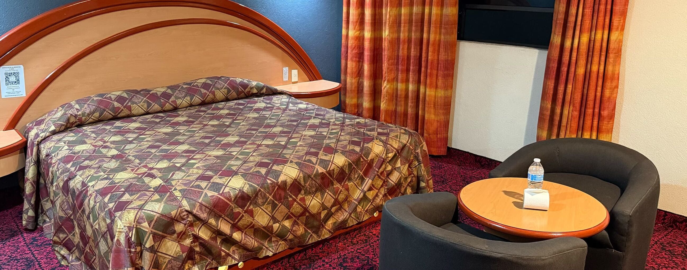 A hotel room with a bed, a chair, a small table, and curtains.
