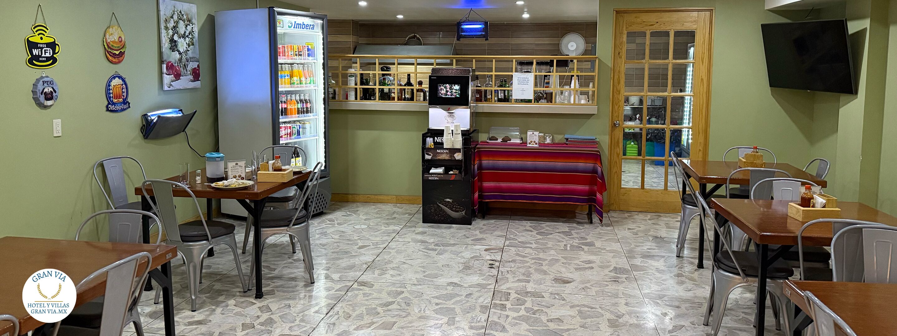 Un restaurante con dispensador de bebidas automático, una barra con diversas opciones de bebidas y un televisor montado en la pared.