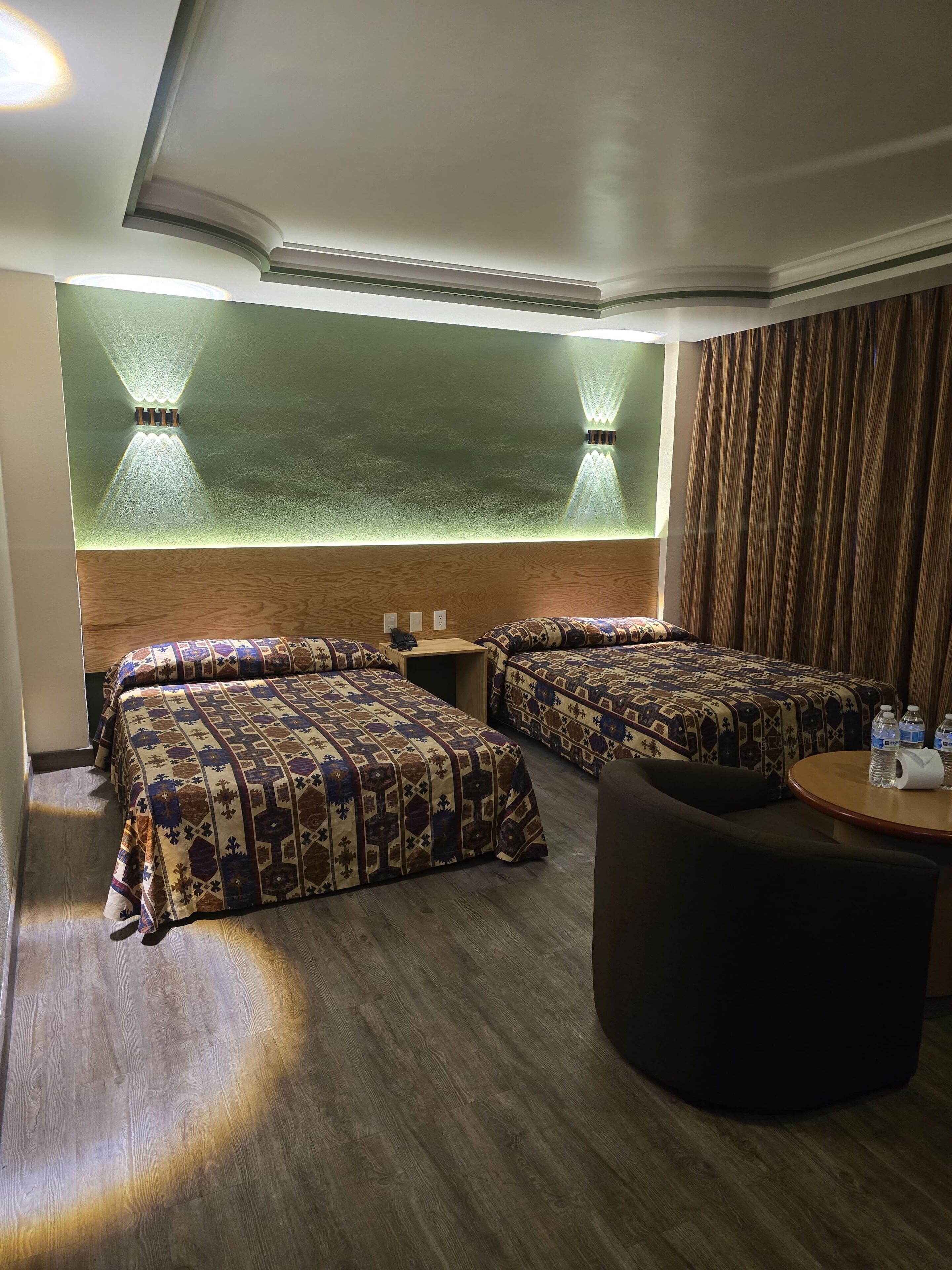 A hotel room with two beds, a round table with water bottles, and a wooden floor.