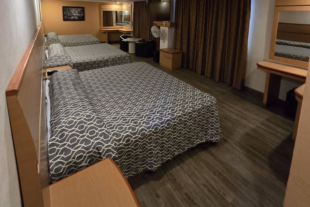 A hotel room with two beds, a desk, a chair, a TV, and a mirror.