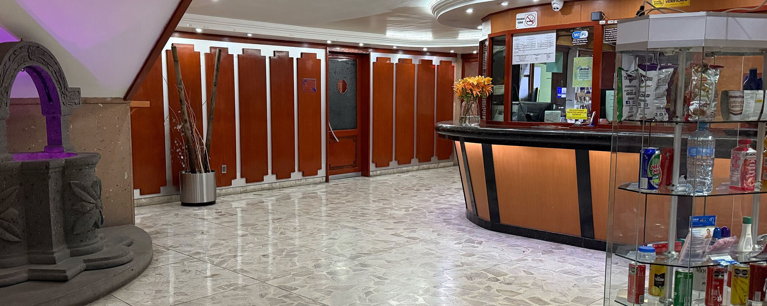 A hotel reception area with a wooden reception desk, a glass display case with toiletries, and a tiled floor.