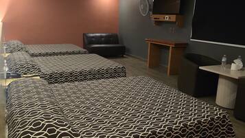 A hotel room with a large bed, a desk, a chair, a TV, and a fan.