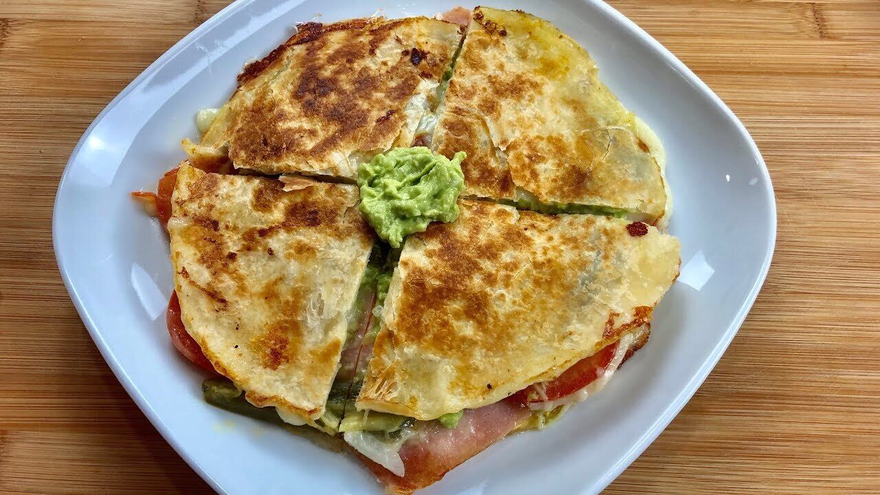 Ein Teller mit einer in vier Stücke geschnittenen Quesadilla, belegt mit Guacamole.