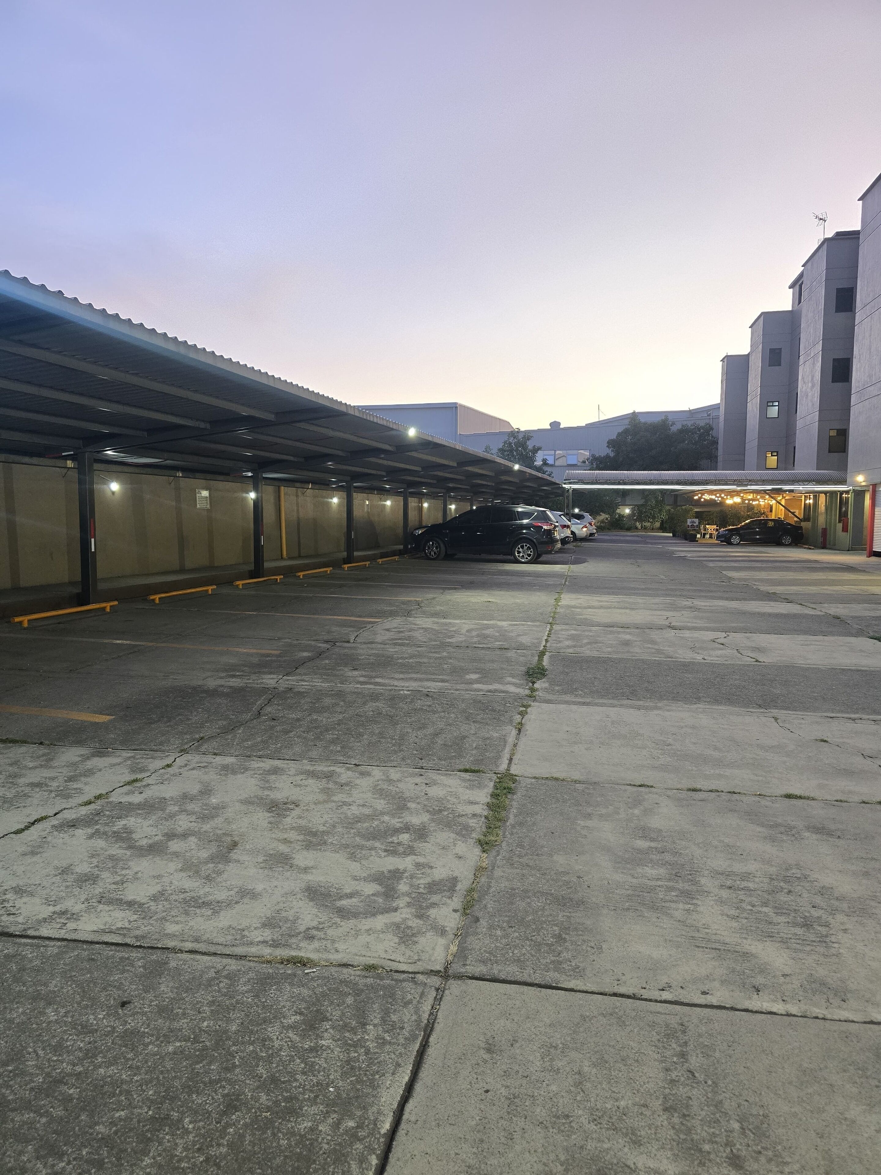 A parking area with a covered section and a building in the background.