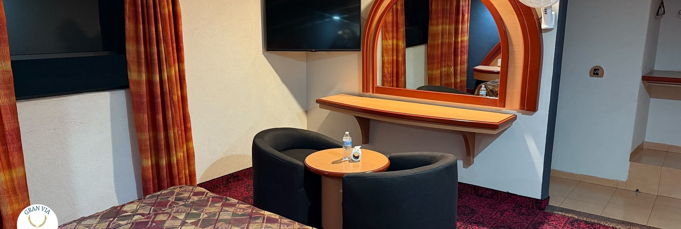 Una habitación de hotel con cama, una mesita con silla, televisión y espejo.