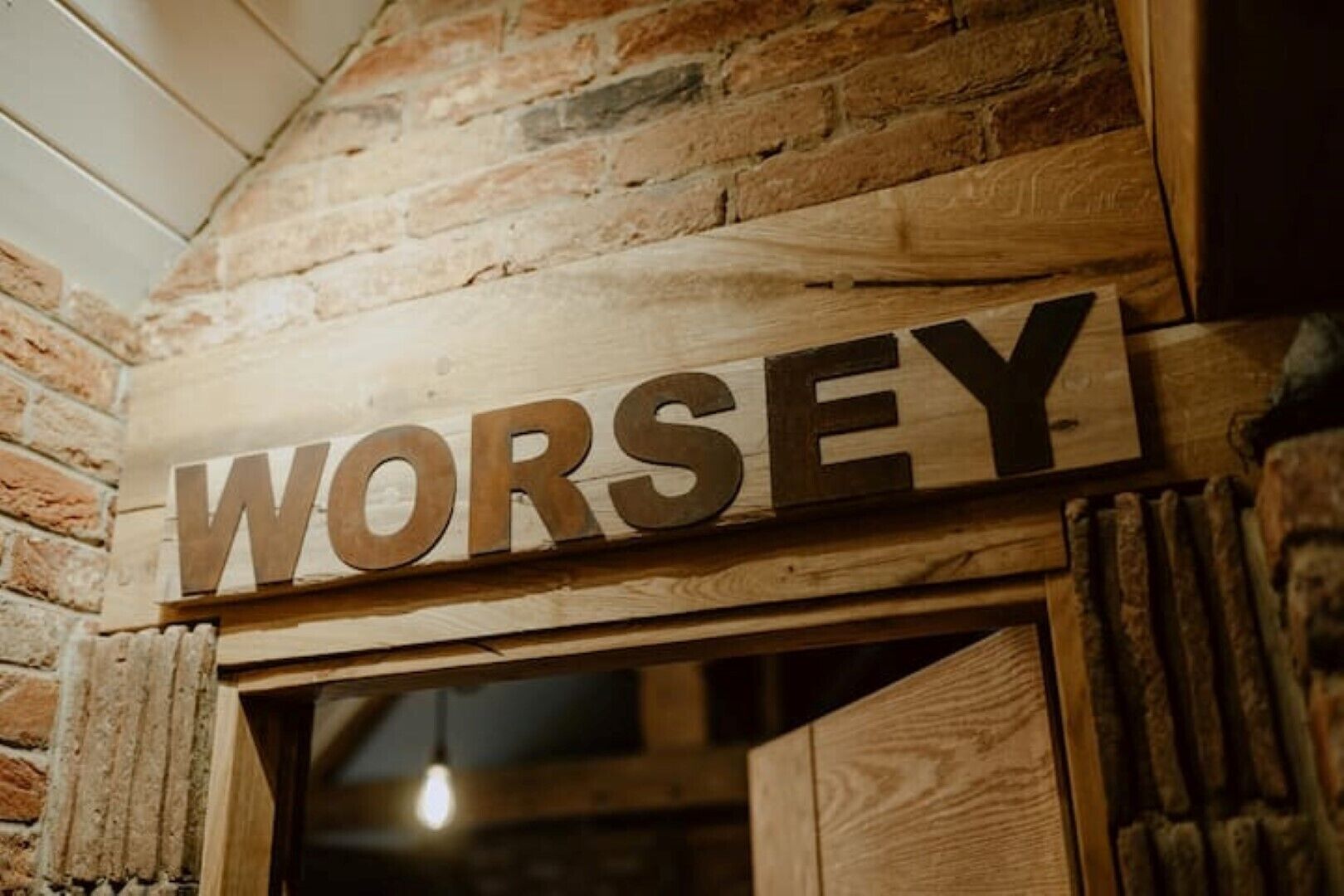 Ein Holzschild mit dem Wort 'WORSEY', an einer Ziegelwand befestigt.