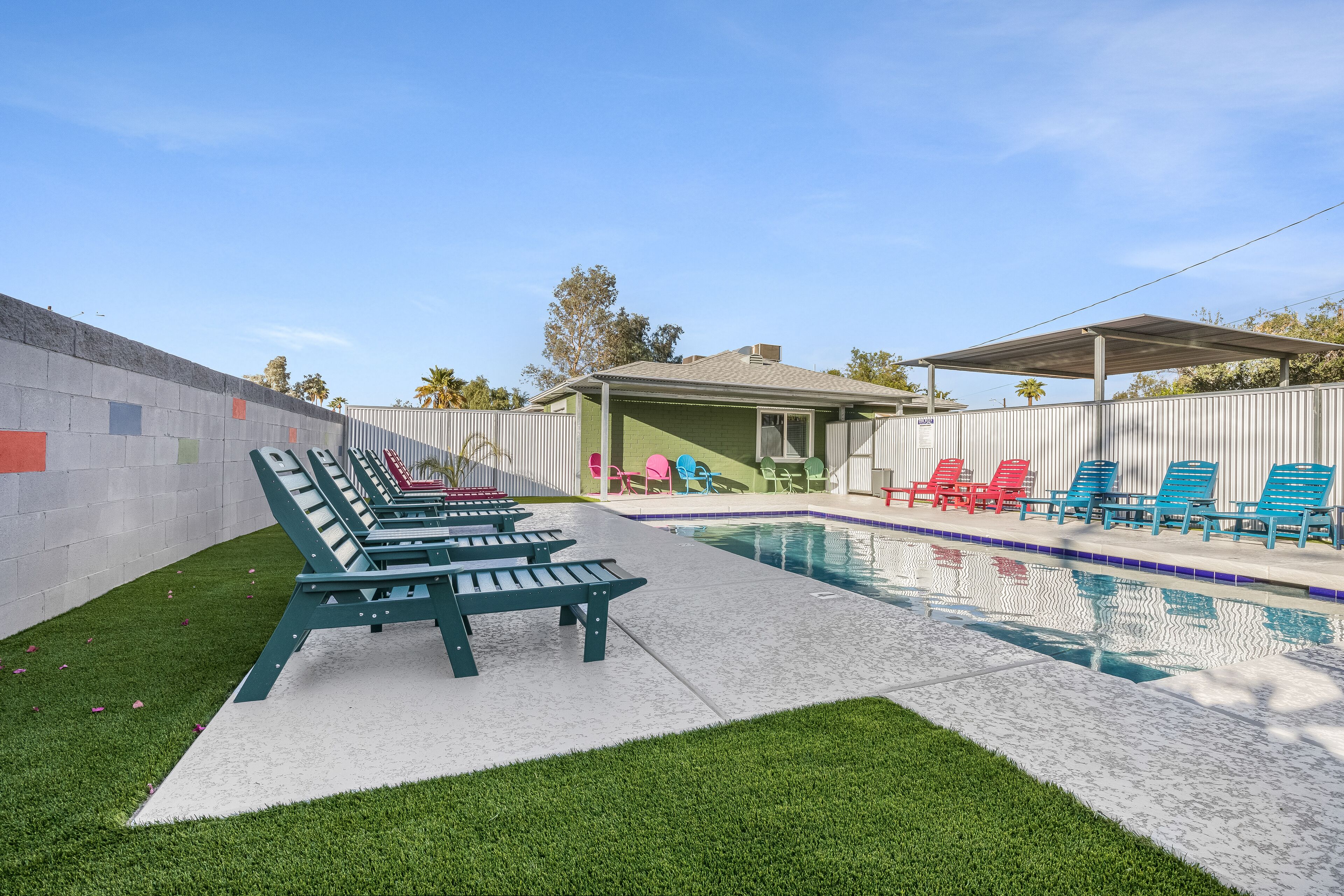 A pool area with green and red lounge chairs, a covered seating area, and a fenced patio.