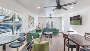 A spacious living area with a green sofa, a dining table, and a ceiling fan. - Biltmore Boho Bungalow w/Heated Pool, Fenced Yard, AC, W/D, Fast Wifi, Smart TVs (Phoenix)