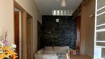 A living room with a stone wall, a sofa, a dining table with chairs, and a vase of flowers.