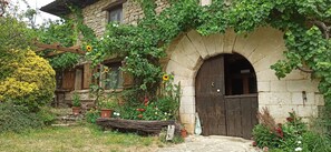 A rustic stone building with a wooden door and a garden with various plants and flowers.