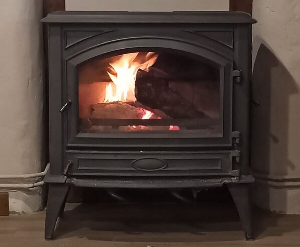A wood-burning stove with a fire burning inside, set in a corner of a room.