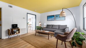 A living room with a sofa, a coffee table, a lamp, and a television. - Coral House - Waterfront Beach Getaway, Stunning Sunsets, 9 min walk to beach! (Wrightsville Beach)