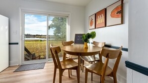 A dining area with a round table and six wooden chairs, a potted plant, and framed artwork on the wall. - Coral House - Waterfront Beach Getaway, Stunning Sunsets, 9 min walk to beach! (Wrightsville Beach)