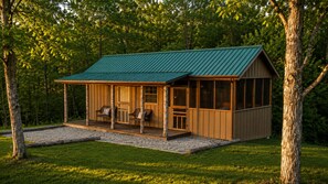 Una baita di legno con tetto verde, un portico con sedie e un’area in ghiaia antistante.