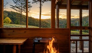 Una baita con interni in legno, un tavolo con un fornello e vista su un paesaggio boschivo.