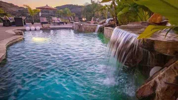A pool with a waterfall feature, surrounded by lounge chairs and a patio area. - The Outside Inn at The Tipsy Goat Ranch (Lakeside)