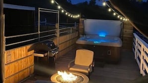 An outdoor patio with a hot tub, seating, and string lights. - The Outside Inn at The Tipsy Goat Ranch (Lakeside)