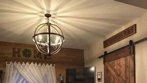 A cozy living room with a stone fireplace, a wooden coffee table, a leather sofa, and a TV mounted on the wall. - The Outside Inn at The Tipsy Goat Ranch (Lakeside)