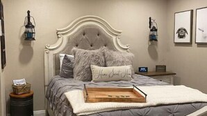 A bedroom with a tufted headboard, a wooden tray on the bed, and two wall-mounted lanterns. - The Outside Inn at The Tipsy Goat Ranch (Lakeside)