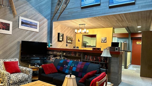 A cozy living room with a sofa, armchairs, a coffee table, and a TV. There are bookshelves with books and a fireplace. - Apex Mountain ~ The Powderhorn (Hedley)