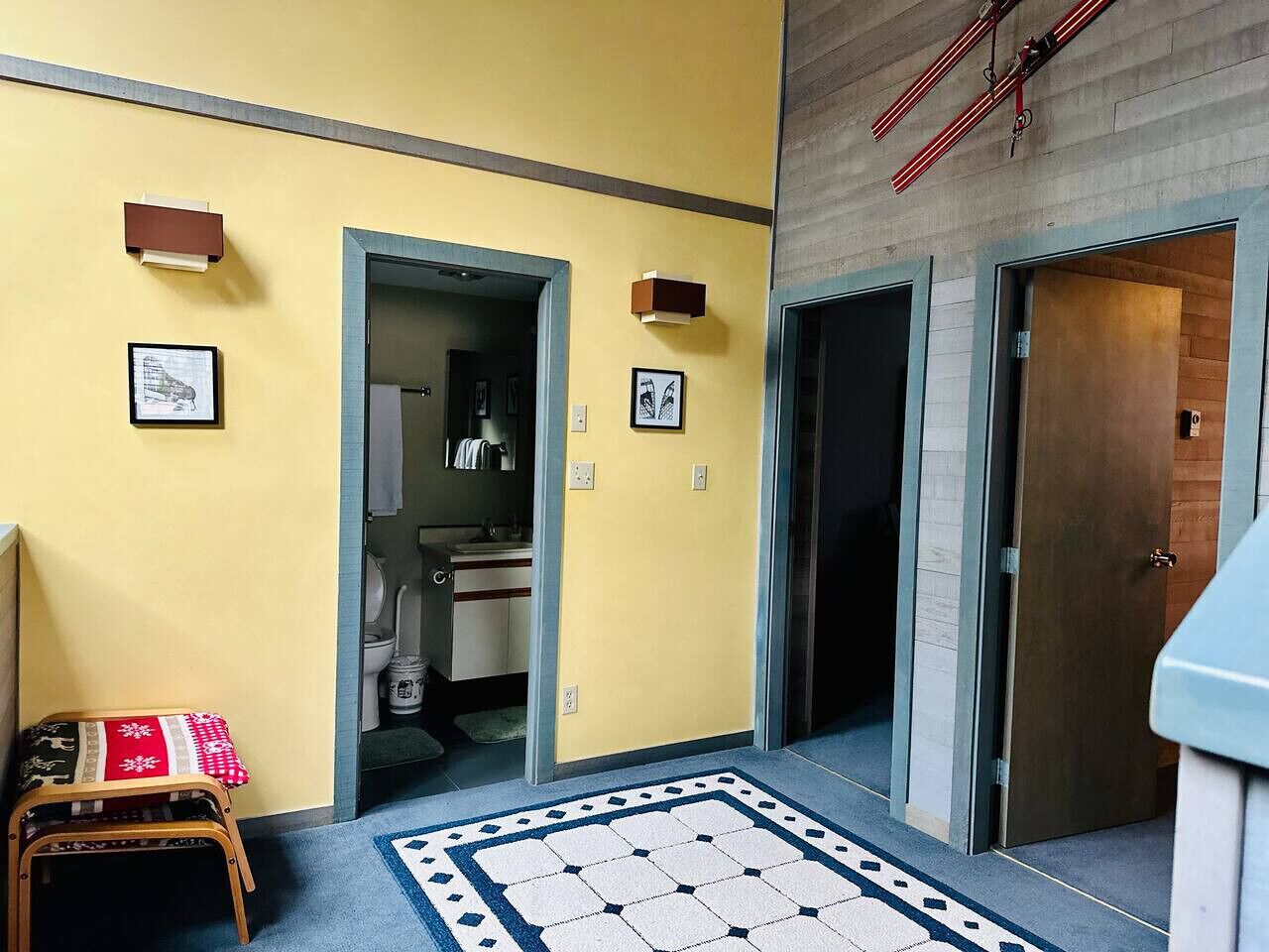 A hallway with a patterned rug, a wooden bench, and a door leading to a bathroom.