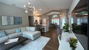 A spacious living room with a sectional sofa, a coffee table, and a dining area with a white table and chairs. - Abacoa/Alton area Heated Pool/Spa Luxury 4Bed Home (Jupiter)