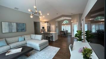 A spacious living room with a sectional sofa, a coffee table, and a dining area with a white table and chairs.