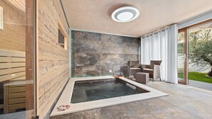 Et moderne spa-område med jacuzzi, stenvægge og en glasdør til en have.