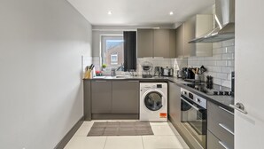 A modern kitchen with a built-in washing machine, a stove, and a sink. - 3br-sleeps8-canarywharf-cinemabedroom (London)