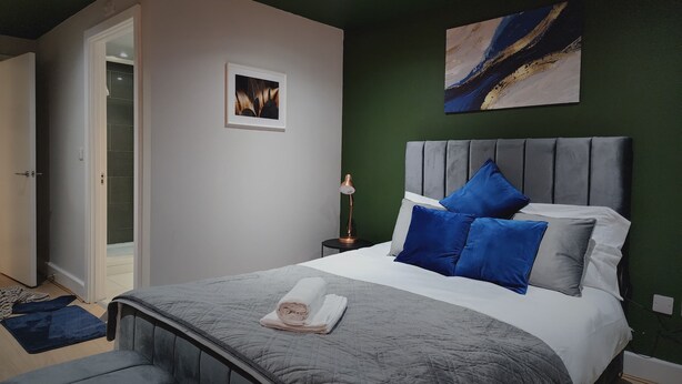 A bedroom with a bed, a nightstand, a lamp, a picture on the wall, and a door leading to another room. - 3br-sleeps8-canarywharf-cinemabedroom (London)