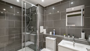 A modern bathroom with a glass-enclosed shower, a white sink, and a mirror above the sink. - 3br-sleeps8-canarywharf-cinemabedroom (London)