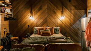A cozy bedroom with a herringbone wooden ceiling, a bed with multiple pillows, a nightstand, and a dresser with a mirror. - Hidden Mountaintop Getaway (Scottsboro)