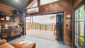 A modern kitchen with a large window, a wooden deck, and a view of the hills. - Hidden Mountaintop Getaway (Scottsboro)