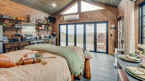 A cozy bedroom with a large bed, a wooden ceiling, and a view of the outdoors through a sliding door. - Hidden Mountaintop Getaway (Scottsboro)