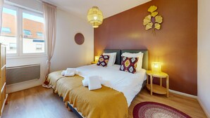 A hotel room with a bed, a bedside lamp, a window with curtains, and a radiator. - Elegance, appartement 6 pers.+ parking (Colmar)