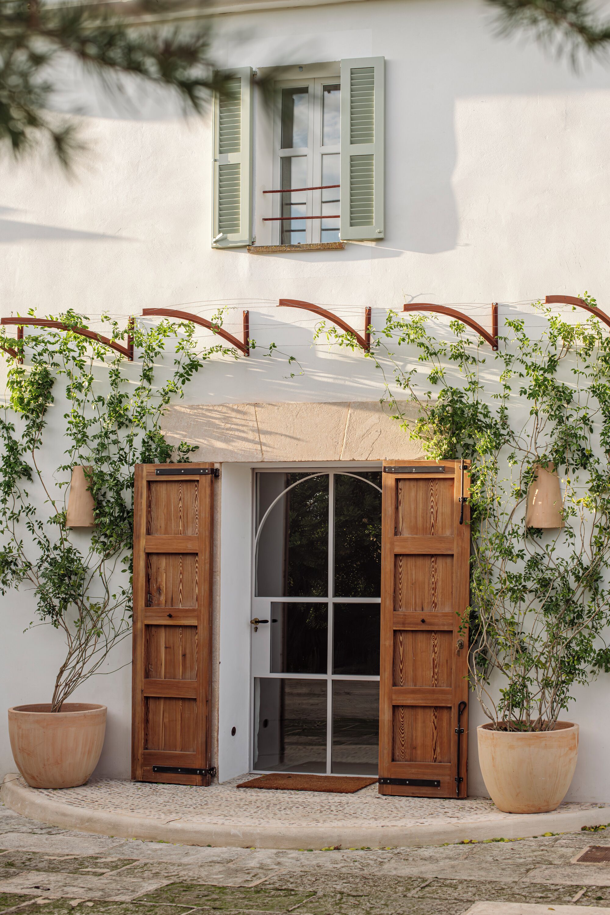 A white building with a wooden door and green shutters, a potted plant, and a small porch area.