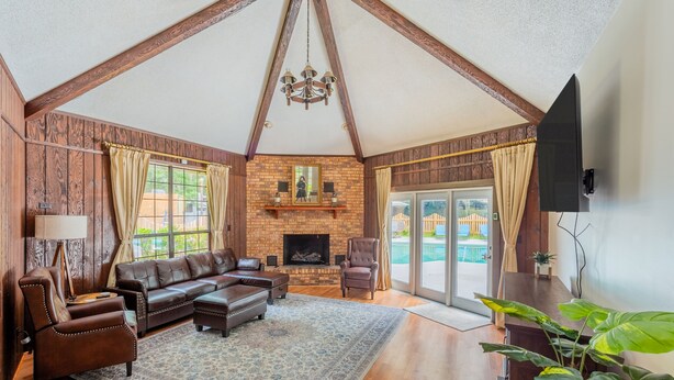 A spacious living room with a fireplace, leather furniture, and a large window overlooking a pool. - Lrge Golden Isles Home-Huge Pool, Hot Tub, Game Rm (Brunswick)