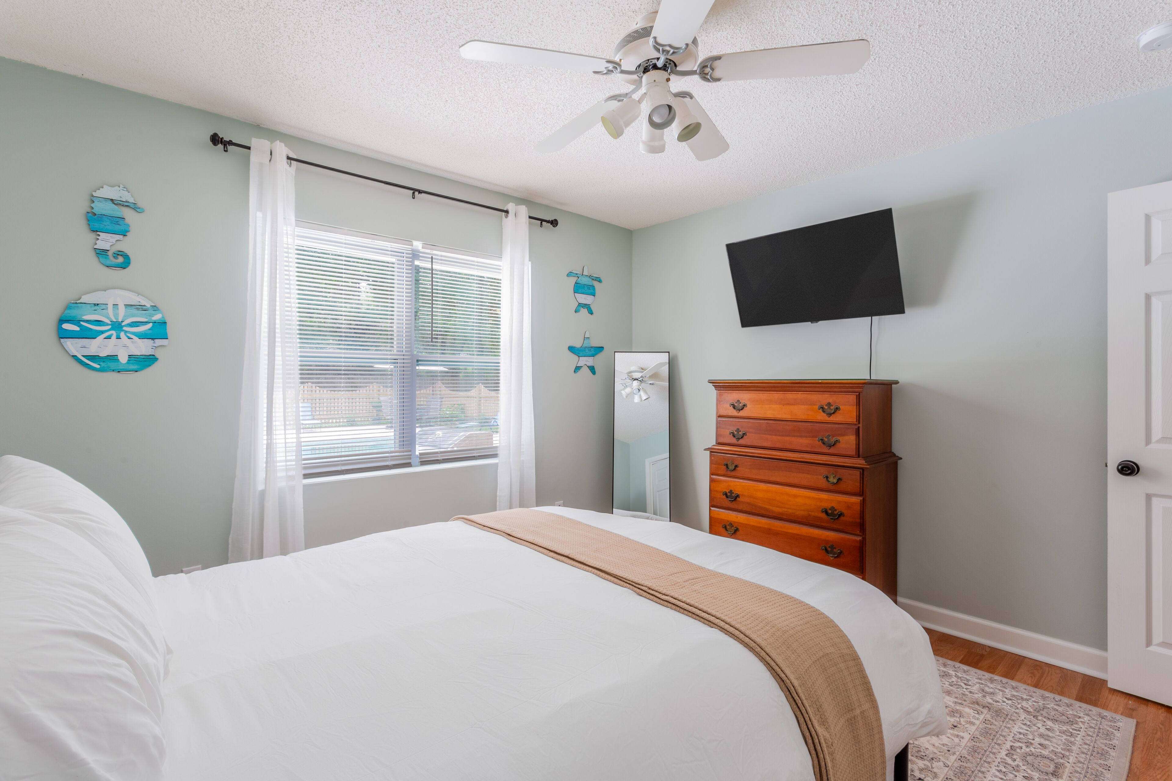 A bedroom with a bed, a ceiling fan, a dresser, and a TV on the wall.