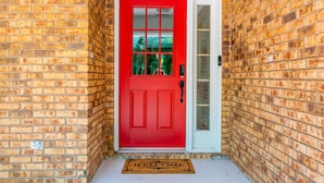 A red door with a white frame, a doormat, and a brick wall. - Lrge Golden Isles Home-Huge Pool, Hot Tub, Game Rm (Brunswick)