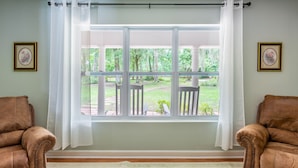 A room with a large window, two brown leather chairs, a green patterned rug, and two framed pictures on the walls. - Lrge Golden Isles Home-Huge Pool, Hot Tub, Game Rm (Brunswick)